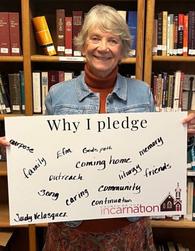 Smiling woman holding 'Why I pledge' sign in library with bookshelves.
