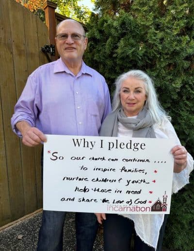 Couple holding a pledge sign outside Church of the Incarnation in front of greenery.